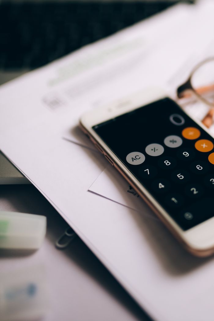 Close-up of a smartphone displaying a calculator app on top of financial documents, indicating business calculations.